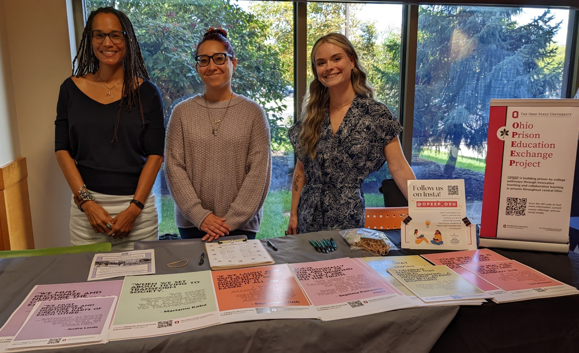 Three woman with pamphlets on a table.