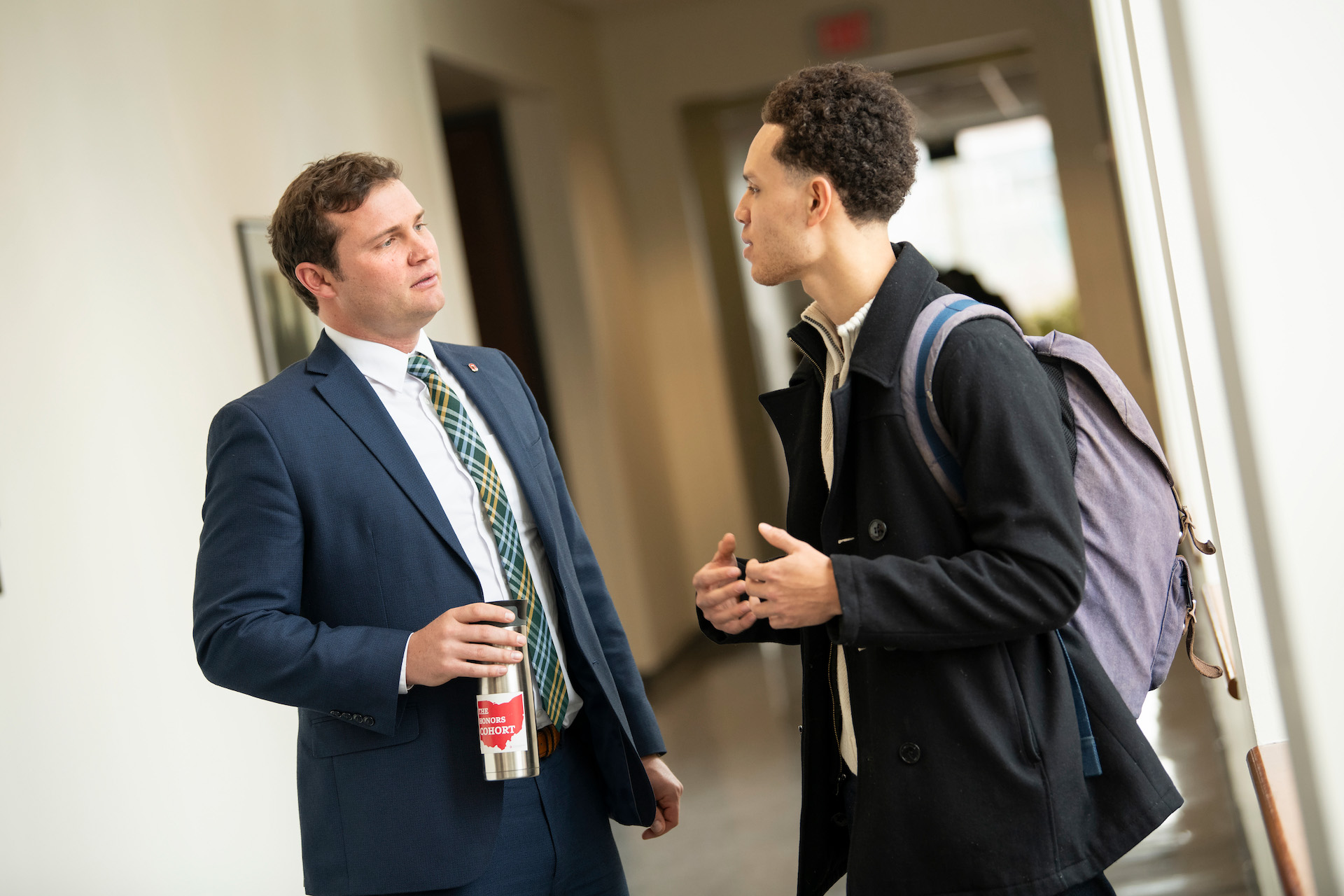 A faculty member speaks with a student in the hallway after class.