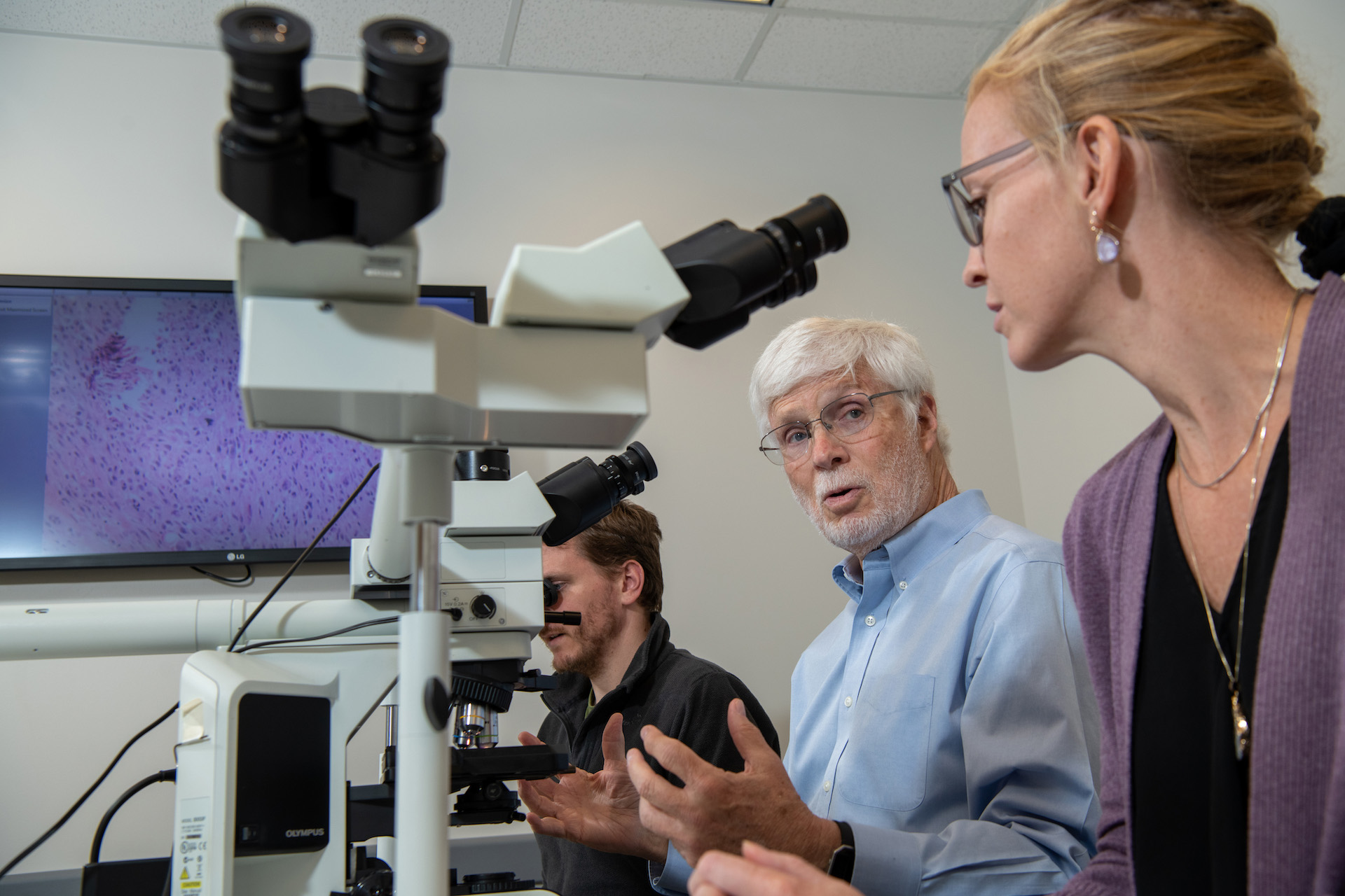Faculty and staff talk in a classroom with microscopes on tables in front of them.