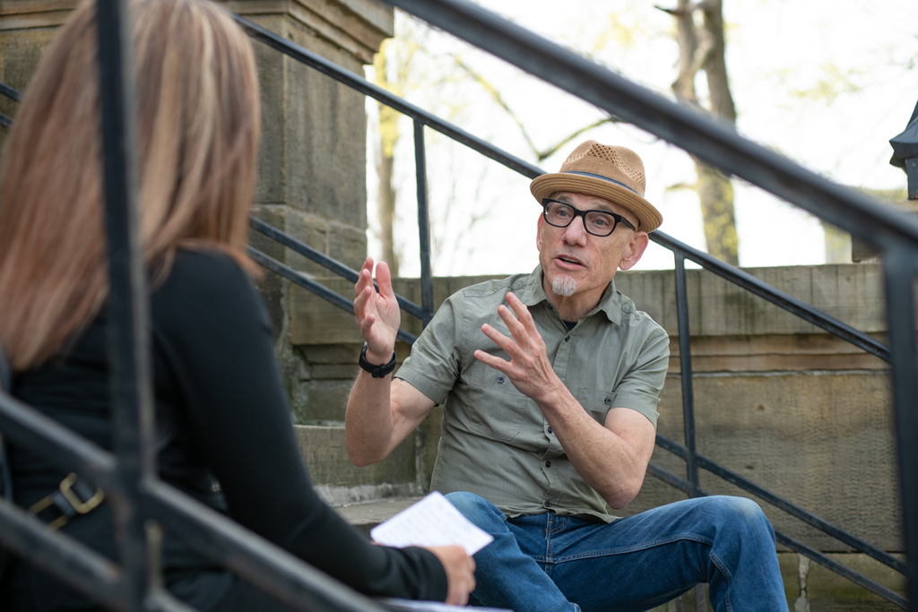 A faculty member speaks to a woman while seated outdoors on concrete steps.
