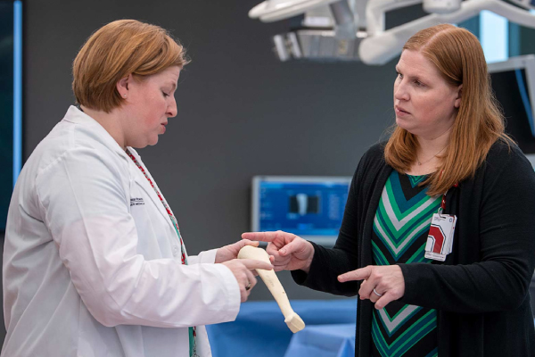 A picture of the Quatman sisters in a medical lab. They are engaged in deep conversation while examining a long, medium sized bone