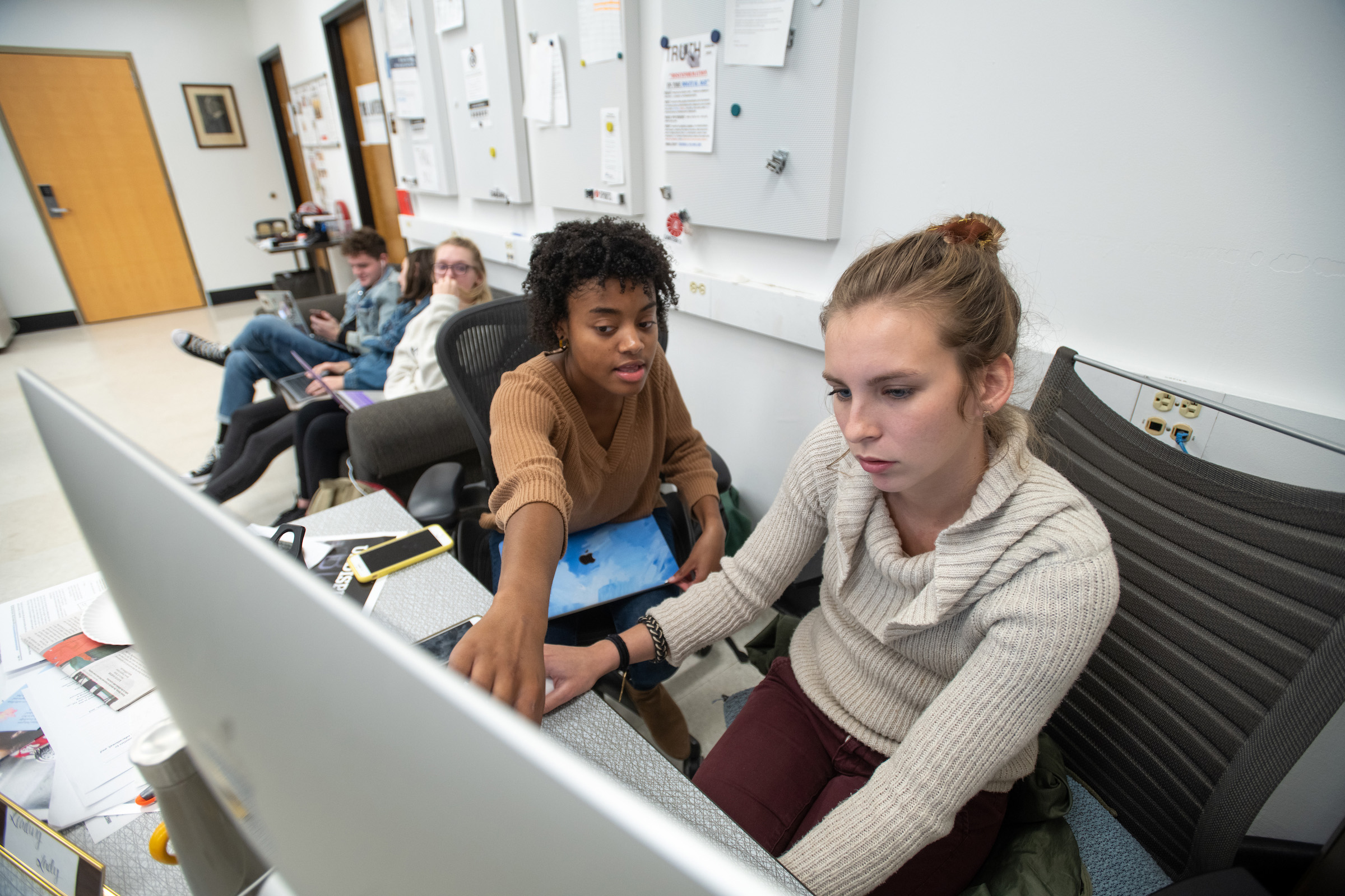 A young black woman professor assists a student on a computer.