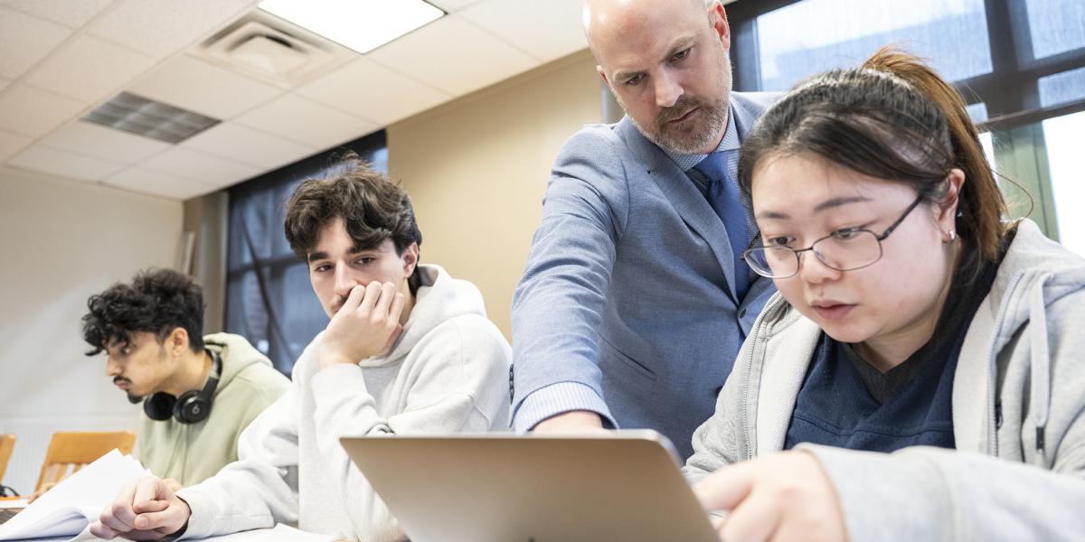 Professor Wallace points to a laptop to help a student, 2 additional students are seated nearby