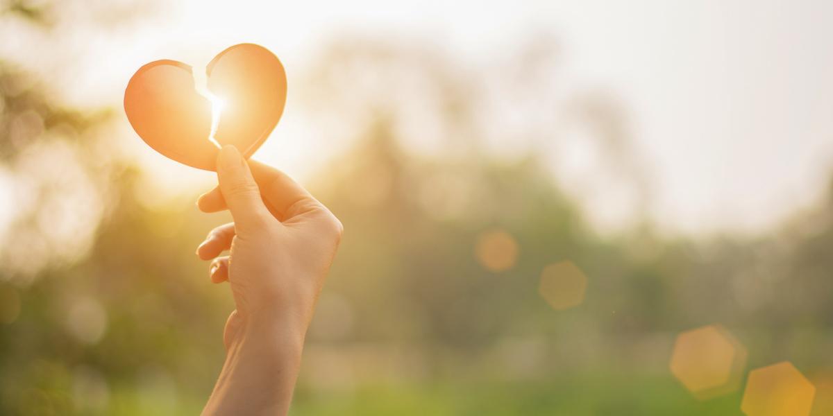 A picture of a hand holding a broken heart up to the sun so that the light shines through.